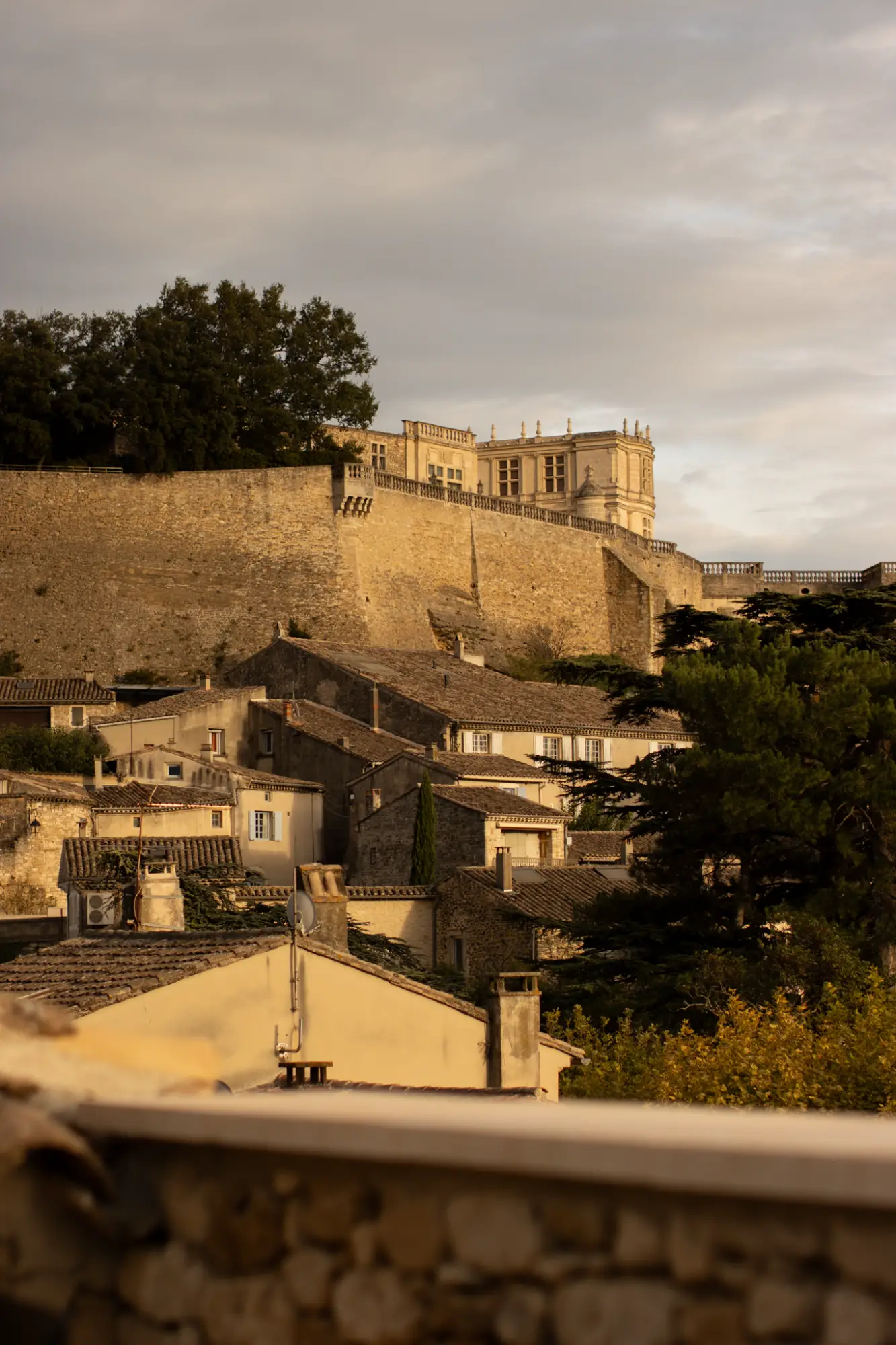 Vue sur un village historique, avec ses toits en pierre et une imposante forteresse en arrière-plan.